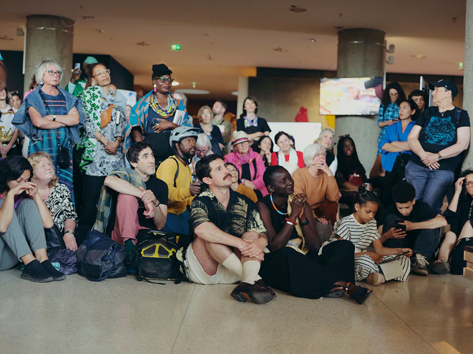 Eine Menschentraube sitzt und steht in einem Ausstellungsraum und blickt nach vorne.